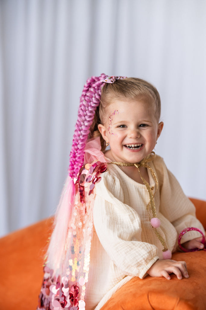 little girl is sitting while in Pink Sequin Cape